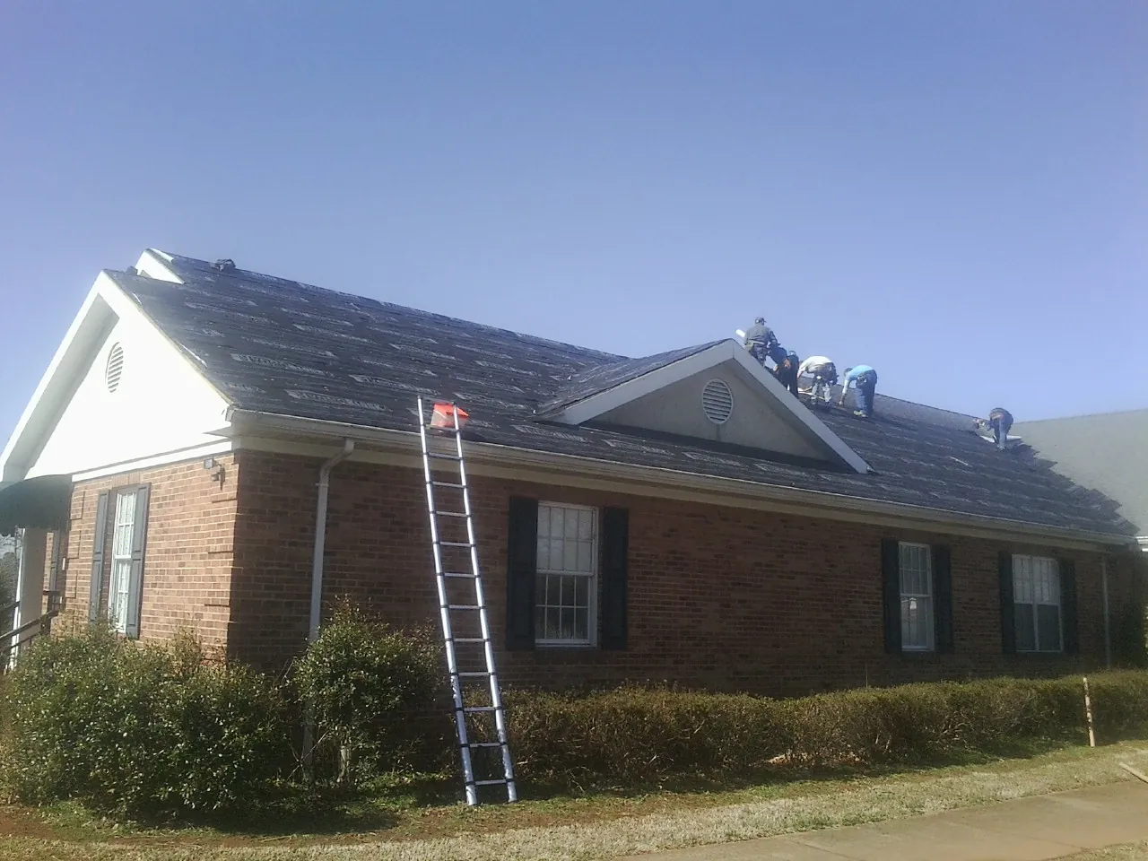 Crew tearing shingles off a brick ranch roof with a ladder set — Metal Roof Repair work by our crew in Lake Villa