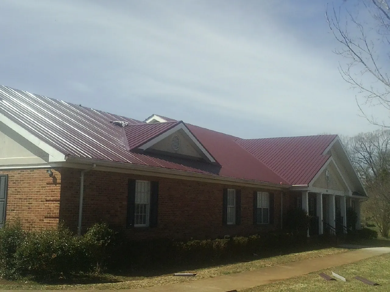 Red metal roof with gabled entries on a long brick building, from a Hail Damage Roof Repair job in Lake Villa