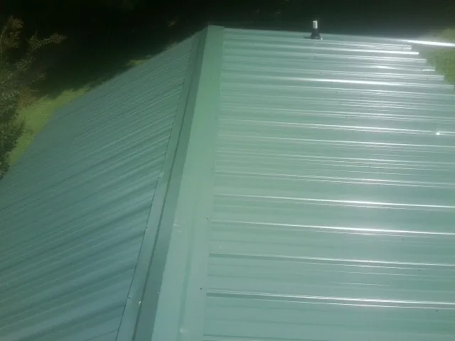 New green metal panels meeting at the ridge of a roof — Flat Roof Repair work by our crew in Lake Villa