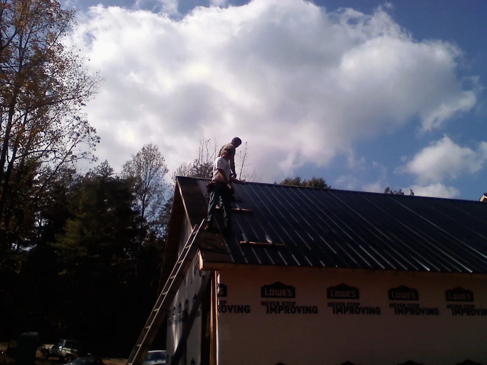 Roofer fastening dark metal panels high against a cloudy sky, from a Roof Inspection job in Lake Villa