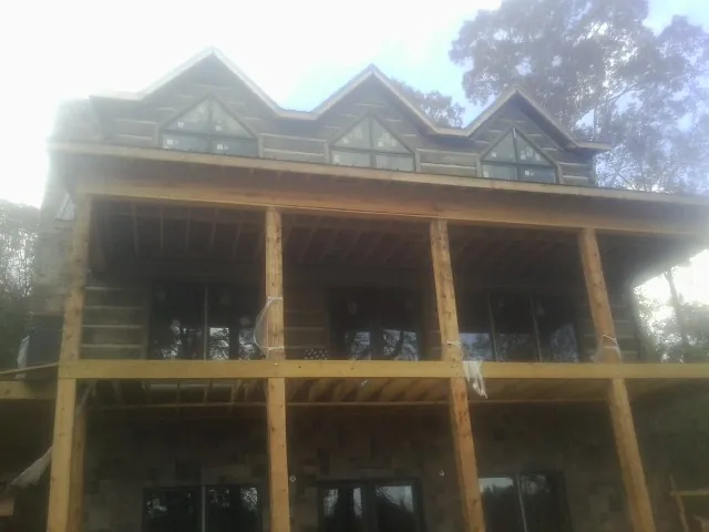 Dormers and porch framing on a large log home under construction — Roof Coating work by our crew in Lake Villa