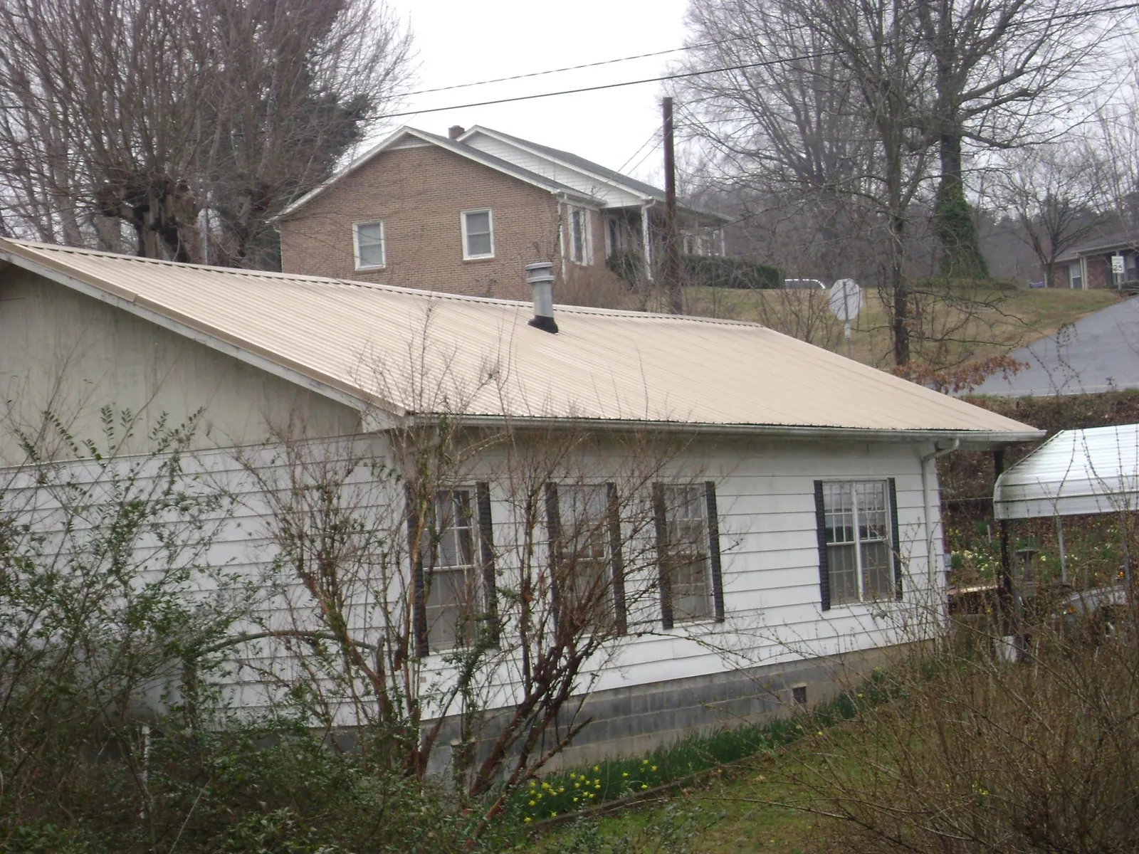 Tan metal roof on a white sided house set into a hillside — Commercial Roofing by Roofing Brothers in Lake Villa